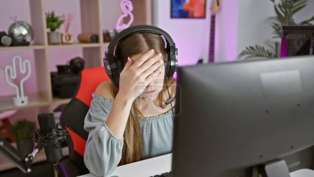 Téléchargez les photos : Une jeune femme stressée dans une salle de jeux, portant un casque, avec un microphone et un ordinateur, à l'intérieur. - en image libre de droit