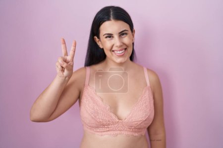 Téléchargez les photos : Jeune femme hispanique portant un soutien-gorge rose montrant et pointant vers le haut avec les doigts numéro deux tout en souriant confiant et heureux. - en image libre de droit