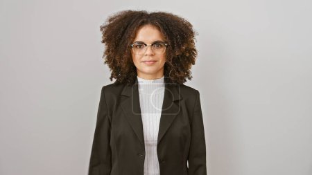 Foto de Joven empresaria hispana confiada con el pelo rizado usando gafas y una chaqueta posa sobre un fondo blanco. - Imagen libre de derechos