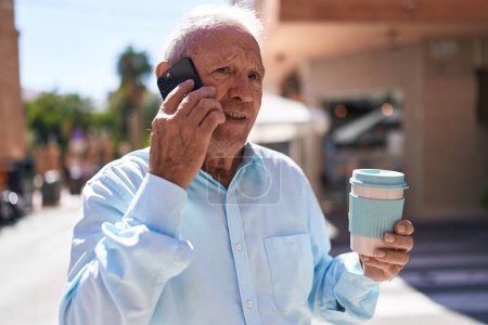 Téléchargez les photos : Moyen Age homme aux cheveux gris parler sur smartphone boire du café à la terrasse du café - en image libre de droit