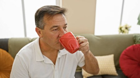 Un homme d'âge moyen profite de son café du matin dans un salon confortable, évoquant un sentiment de confort à la maison.