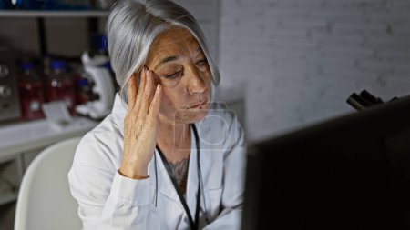 Foto de Científica de cabello gris de mediana edad, rostro enfocado iluminado por el resplandor de las computadoras, trabajando diligentemente en la investigación revolucionaria en un laboratorio silencioso - Imagen libre de derechos