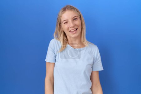 Téléchargez les photos : Jeune femme caucasienne portant casual bleu t-shirt clin d'oeil en regardant la caméra avec une expression sexy, gai et heureux visage. - en image libre de droit
