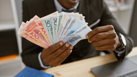 Téléchargez les photos : Homme africain comptant le yuan chinois dans un cadre de bureau moderne, dépeignant la finance et la diversité sur le lieu de travail. - en image libre de droit