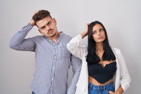 Photo for Young hispanic couple standing over white background confuse and wondering about question. uncertain with doubt, thinking with hand on head. pensive concept. - Royalty Free Image