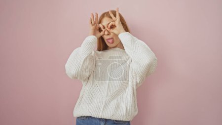 Photo for Playful young woman making glasses with fingers over her eyes against a pink background, embodying joy and youthfulness. - Royalty Free Image