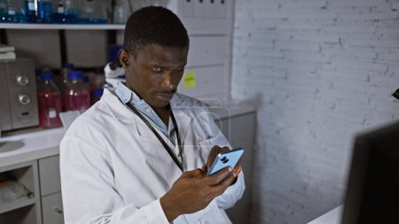 African man in labcoat using smartphone in laboratory