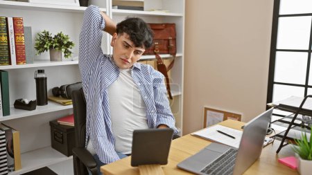 Téléchargez les photos : Un jeune homme s'étire pendant une pause dans un bureau moderne, affichant des vêtements d'affaires décontractés et de la technologie autour. - en image libre de droit