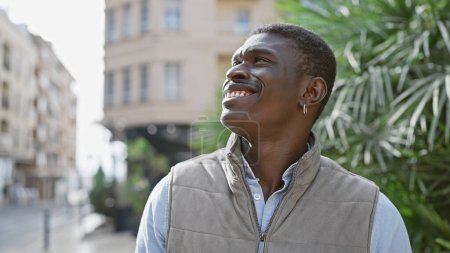 Téléchargez les photos : Homme africain souriant profitant du plein air dans un environnement urbain, respirant la confiance et le style décontractés. - en image libre de droit