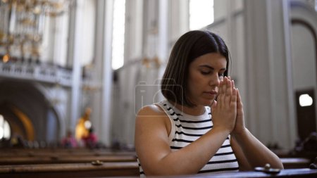 Junge schöne hispanische Frau betet auf einer Kirchenbank in der Augustinerkirche in Wien