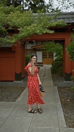 Hello, japan! confident and beautiful hispanic woman in glasses extends a friendly wave invite at gotokuji temple, tokyo's lucky cat maneki-neko home.