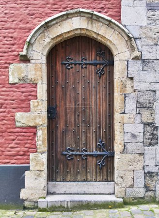 Téléchargez les photos : Ancienne porte en bois avec charnières en fer sur un mur rouge texturé, typique de l'architecture médiévale européenne. - en image libre de droit