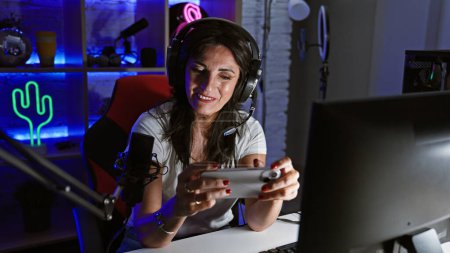 Téléchargez les photos : Femme souriante jouant à des jeux dans une pièce sombre avec une lumière au néon colorée. - en image libre de droit