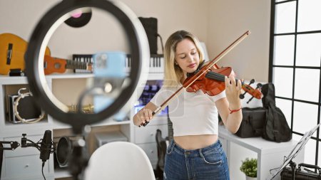 Téléchargez les photos : Jeune femme blonde musicienne enregistrement vidéo jouer du violon au studio de musique - en image libre de droit