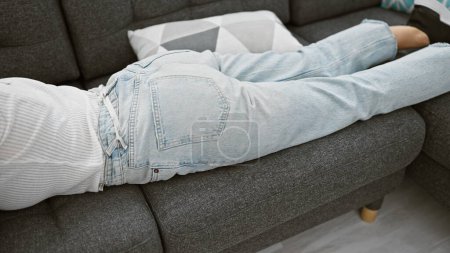 Téléchargez les photos : Femme décontractée se relaxant sur un canapé gris à l'intérieur, évoquant un sentiment de confort à la maison et de loisirs. - en image libre de droit