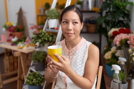 Téléchargez les photos : Young asian woman florist smiling confident drinking cup of coffee at flower shop - en image libre de droit