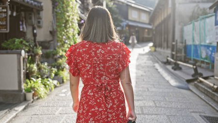 Foto de El paseo casual de la hermosa mujer hispana por la antigua calle Gion de Kyoto capta el ojo, su cabello moreno fluyendo, la vista posterior presentada tradicionalmente en el retrato de un adulto yong, Japón, Asia - Imagen libre de derechos