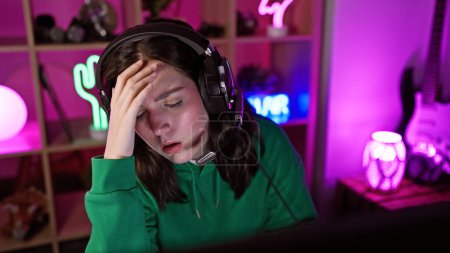 Photo for A stressed young woman gamer in headphones experiencing defeat in a colorful neon-lit gaming room at night. - Royalty Free Image