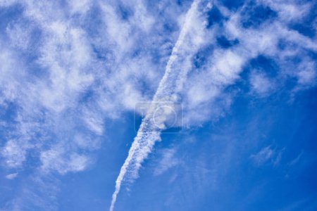 A clear blue sky intercepted by a stark contrail, hinting at distant travel and vast atmosphere.