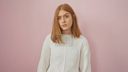 Photo for Serene young woman with red hair wearing a white sweater isolated against a pink background, evoking subtlety and elegance. - Royalty Free Image