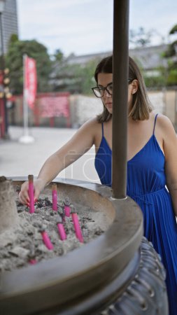 Téléchargez les photos : Belle jeune femme hispanique portant des lunettes tenant un bâton d'encens au temple du parc ueno - en image libre de droit