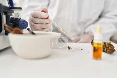 Téléchargez les photos : Jeune homme latin scientifique versant du liquide sur un échantillon d'herbe de cannabis au laboratoire - en image libre de droit