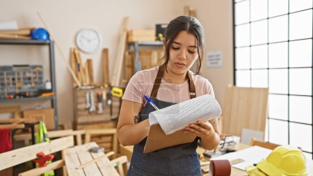A young hispanic woman reviews plans in a well-equipped carpentry workshop, indicating a hands-on creative occupation.