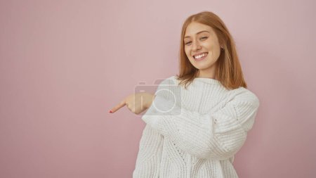 Photo for A smiling young caucasian woman points downwards against a pink isolated background, projecting a casual and approachable vibe. - Royalty Free Image