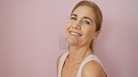 Foto de Una sonriente mujer caucásica, madura posando sobre un fondo rosa aislado, exudando confianza y belleza. - Imagen libre de derechos