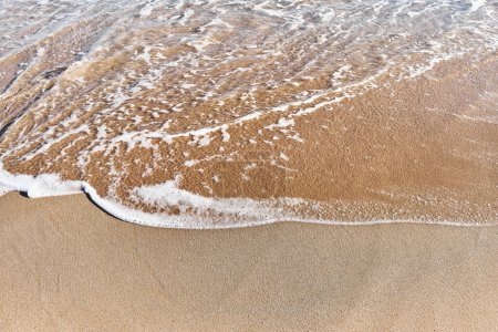 Sanfte Wellen spülen über den goldenen Sand an einem ruhigen Strand, der Ruhe und die Einfachheit der Natur symbolisiert.