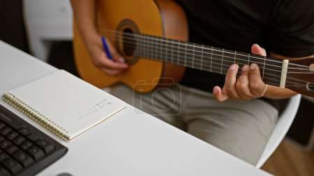 Foto de Apasionado joven latino, un músico en el corazón de su oficio, componiendo una melodía mientras sostiene una guitarra clásica en un acogedor estudio de música - Imagen libre de derechos