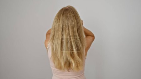 Téléchargez les photos : Femme blonde par derrière sur un fond blanc, mettant en valeur ses cheveux longs et son haut rose. - en image libre de droit