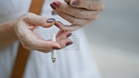 Foto de Primer plano de los dedos de una mujer adulta sosteniendo un cigarrillo sobre un fondo urbano de la calle - Imagen libre de derechos