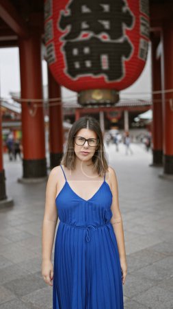 Photo for Confident and beautiful hispanic woman expressing a serious gesture through her glasses as she stands, deep in thought, at the iconic red senso-ji shrine in asakusa, tokyo. - Royalty Free Image