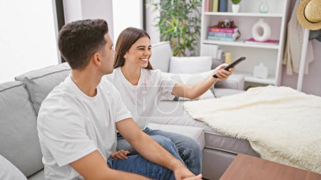 A woman and man share a joyful moment while sitting on a couch in a cozy living room, watching television together.