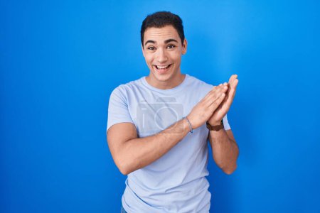Téléchargez les photos : Young hispanic man standing over blue background clapping and applauding happy and joyful, smiling proud hands together - en image libre de droit