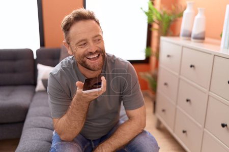 Photo for Middle age man talking on the smartphone sitting on sofa at home - Royalty Free Image