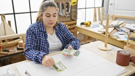 Hispanic woman counting bangladesh currency in a carpentry workshop