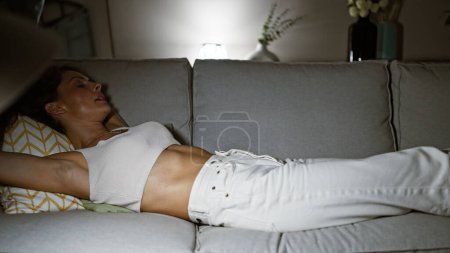 Eine junge Frau entspannt auf einem Sofa in einer lässigen, gemütlichen Wohnzimmeratmosphäre und verkörpert Ruhe und Komfort.