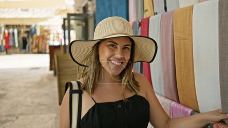 Foto de Una joven sonriente en un sombrero de ala ancha comprando en un zoco tradicional en Dubái. - Imagen libre de derechos