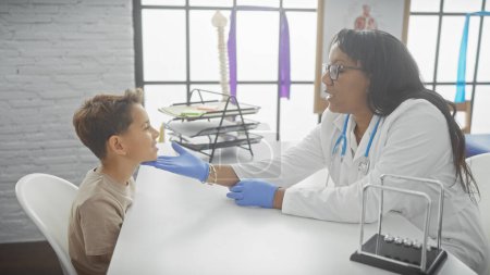 Téléchargez les photos : Une femme médecin s'engage avec un jeune garçon dans une salle d'examen pédiatrique, symbolisant les soins de santé, la confiance et le professionnalisme. - en image libre de droit