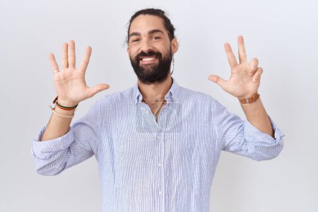 Foto de Hombre hispano con barba vistiendo camisa casual mostrando y señalando con los dedos número ocho mientras sonríe confiado y feliz. - Imagen libre de derechos