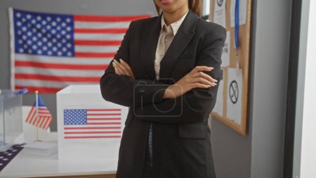 Téléchargez les photos : Une femme afro-américaine confiante aux bras croisés se tient dans une salle d'université électorale, incarnant le leadership et la démocratie américaine. - en image libre de droit