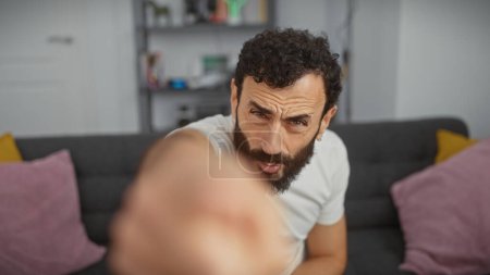 Foto de Hombre guapo de mediana edad con barba extendiendo la mano hacia la cámara en la sala de estar moderna. - Imagen libre de derechos