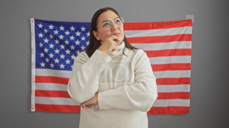 Thoughtful mature hispanic woman in office with usa flag in background