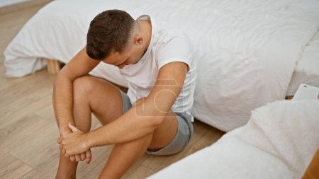 Nachdenklicher junger Mann sitzt auf dem Fußboden eines Schlafzimmers und reflektiert inmitten einer ruhigen inneren Umgebung