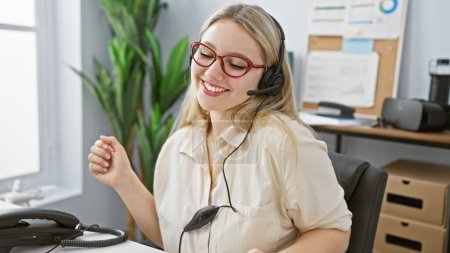 Photo for Cheerful young woman wearing headset in office with computer and files, embodying professional customer service. - Royalty Free Image