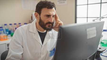 Téléchargez les photos : Homme concentré avec barbe en blouse de laboratoire analysant les données sur ordinateur dans un laboratoire de recherche - en image libre de droit