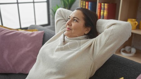 Téléchargez les photos : Une femme hispanique détendue se prélasse à la maison, rêvant sur un canapé confortable dans un salon bien décoré. - en image libre de droit