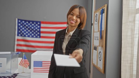 Foto de Una sonriente mujer afroamericana emitiendo su voto en un colegio electoral estadounidense. - Imagen libre de derechos